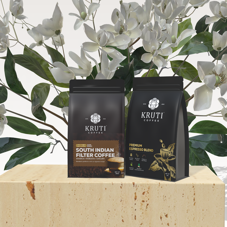 Two packets of Kruti Coffee, one labeled as 'South Indian Filter Coffee' and the other as 'Premium Blend', against a background with white flowers and green leaves.